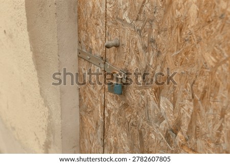 Angled view padlock on chipboard near plaster wall, metal latch secured with rust, soft daylight, construction site ambience and quiet urban closure
