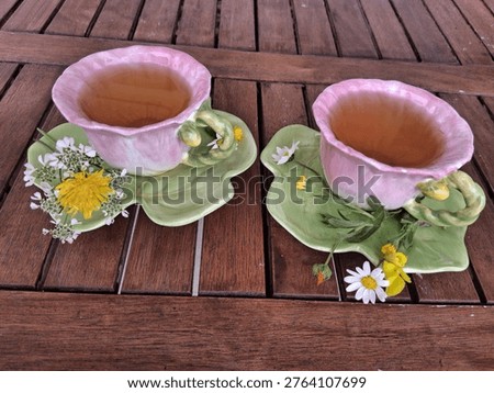 Angled view of two artistic tea cups shaped like pink blossoms, filled with green organic tea and placed on leaf-inspired saucers.