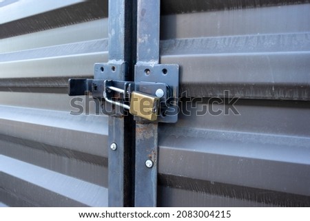 Angled view of a yellow padlock keeping two large metal doors locked up tight in an outdoor storage facility