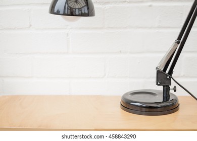 Anglepoise Lamp. Black Retro Table Top Light On Wooden Desk With White Brick Background. Space For Text.