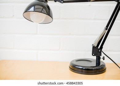 Anglepoise Lamp. Black Retro Table Top Light On Wooden Desk With White Brick Background. Space For Copy