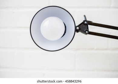 Anglepoise Lamp. Bulb And Light In Mid Frame With White Brick Background.