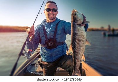 Angler with Asp fish. Amateur fisherman holds the asp fish and stands in the boat with river on the background - Powered by Shutterstock