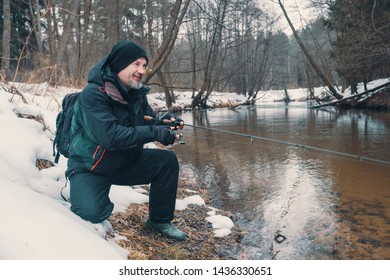 Angler With A Rod On The River Bank. Fishing For Trout. Winter Spinning.