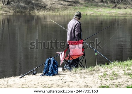 The angler sits on the bank of the river and fishes. Recreation by nature, fishing like a soothing hobby. Nature's Therapy: Angler Finds Peace Along the Riverbank.  