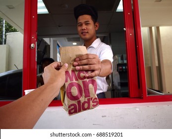 ANGONO, RIZAL, PHILIPPINES - JULY 29, 2017: A Fast Food Chain Worker Hands Over An Order Of Food To A Customer At A Drive Thru Counter.