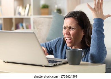 Angry adult woman watching video online on laptop sitting on the floor at home