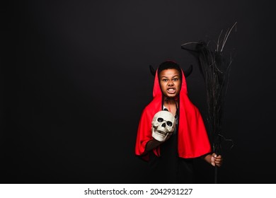 Angry African American Boy Holding Broom And Skull While Grinning Isolated On Black