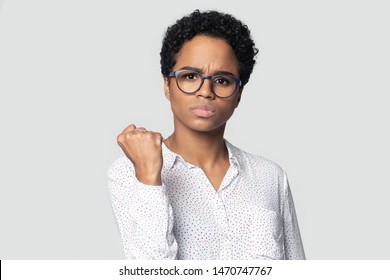 Angry african american serious girl looking at camera, clenching fist, demonstrating power, isolated on grey studio background. Annoyed strong ethnic woman giving warning, head shot close up portrait. - Powered by Shutterstock