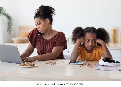 Angry African American Teen Girl Sitting By Working Mom, Need For Attention, Kitchen Interior. Busy Black Lady Working From Home, Using Laptop And Having Phone Conversation, Have No Time For Kid