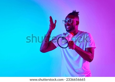 Angry african-american man in glasses shouting in megaphone and holding one hand up over gradient colorful background in neon. Concept of people, emotions, expression, job, ad