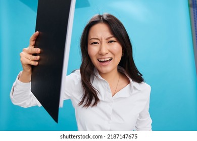 Angry Aggressive Cute Asian Businesswoman In Classic Office Dress Code Throwing Folder Tablet At Camera Posing Isolated On Over Blue Studio Background. Cool Business Offer. Job Interview Concept