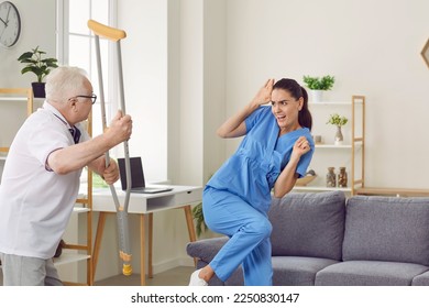 Angry aggressive elderly man threatening to his caregiver woman. Elderly patient suffering from mental disability threatening with crutch to frightened nurse. Professional medical help and support - Shutterstock ID 2250830147