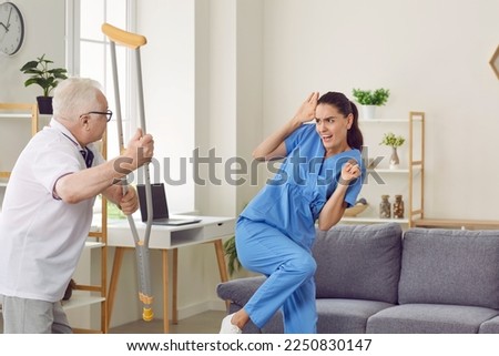 Angry aggressive elderly man threatening to his caregiver woman. Elderly patient suffering from mental disability threatening with crutch to frightened nurse. Professional medical help and support