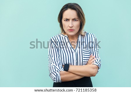 Angry, aggressive. Handsome elegant woman looking at camera with angry face . Studio shot, on light blue background.