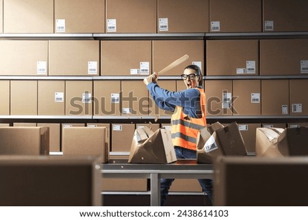 Angry aggressive warehouse worker hitting cardboard boxes with a bat, burnout and rage concept