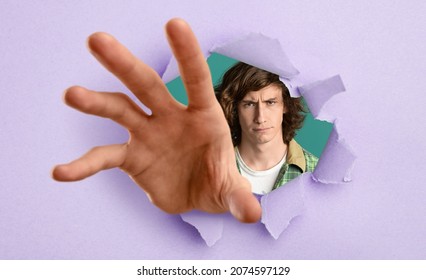 Angry agressive teenage guy reaching through hole in torn violet paper, trying to grab something. Frustrated Caucasian teen grasping, trying to start fight, feeling annoyed, panorama
