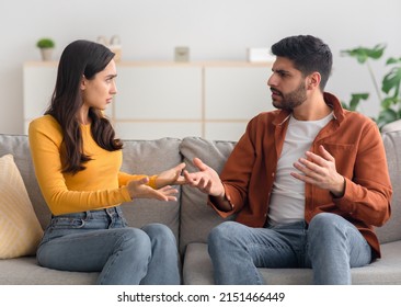 Angry Arabic Spouses Having Quarrel Arguing Looking At Each Other Sitting On Couch At Home. Domestic Violence And Abuse. Couple Struggling From Marital Crisis Concept