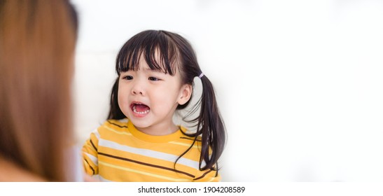 Angry Asian Kid.Little Asian Girl Looking At Her Mother And Fighting With Her Mom.Furious Hungry Toddler Kid Got Upset And Sad.Stubborn Child Bad Attitude.Depressed Little Girl Complaining With Mom.