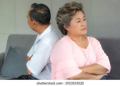 Angry Asian Senior Couple Sitting On Sofa Together But Back To Back Looking To Opposite Sides.  Two Elderly Arguing Concept