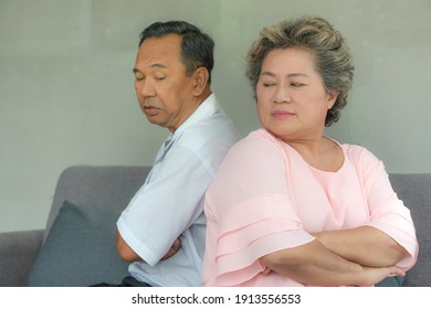 Angry Asian Senior Couple Sitting On Sofa Together But Back To Back With Unhappy Faces.  Two Elderly Arguing Concept