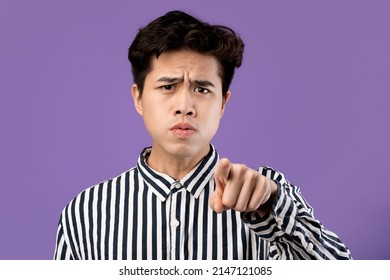 Angry Asian Teenager Frowning And Pointing Index Finger At Camera On Purple Violet Studio Walll. Furious Male Adolescent Feeling Irritated, Blaming You. Facial Expression, Negative Emotions Concept