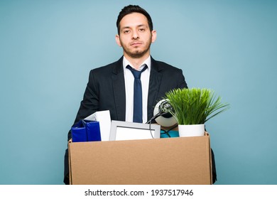 Angry Attractive Man Wearing A Black Suit And Holding A Brown Box With His Office Supplies. Upset Man Got Fired From An Office Job