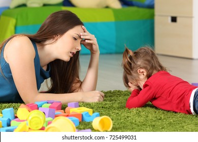 Angry baby and tired mother lying on a carpet in a room
