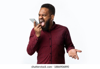 Angry Black Guy Shouting At Smartphone Talking By Phone Standing Over White Studio Background. Anger, Negative Emotion. Discontented Customer Having Quarrel By Cellphone