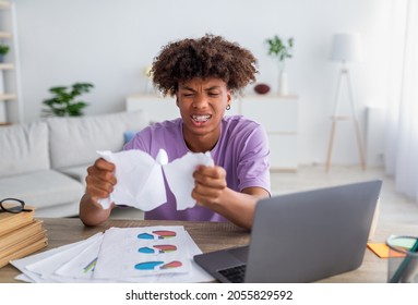 Angry Black Teenager Tearing Down His Coursework Paper Near Laptop At Home. African American Youth Not Understanding New Material During Online Education, Feeling Desperate Indoors