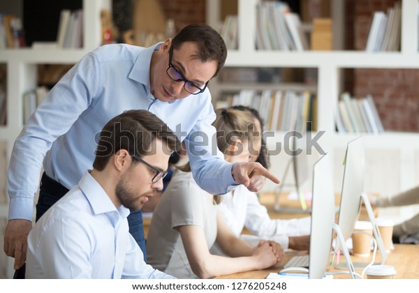 Angry boss criticizing scolding sad male employee\
for computer mistake incompetence at workplace, mad leader\
reprimanding rebuking shouting at subordinate lazy worker blaming\
of bad work in office