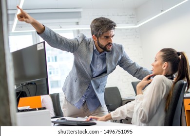 Angry Boss Firing Upset Female Employee In Office. Young Male Business Manager Yelling At Scared And Stressed Business Woman At Her Workplace.