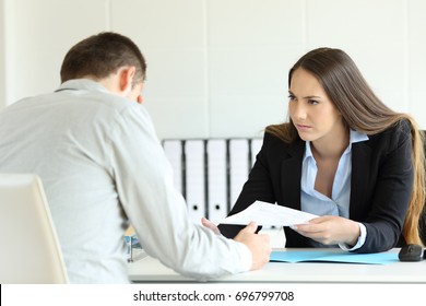 Angry Boss Giving A Document To A Sad Employee Sitting In A Desk At Office