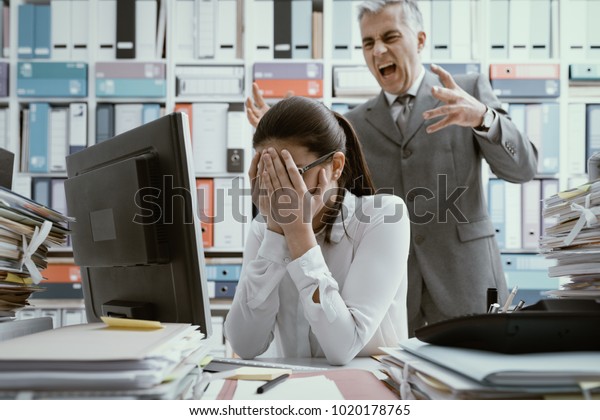 Angry boss\
yelling at his young employee, she is stressed and feeling\
frustrated: bullying boss and mobbing\
concept