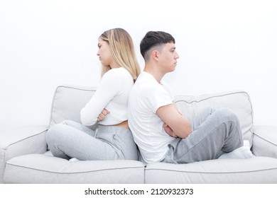 Angry Boy And Girl Sitting In The Sofa Back To Back. Young Couple At Home. Heterosexual 18-20 Years Old Couple.