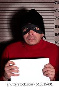 Angry Burglar In Red Sweater, Black Hat And Mask Holding White Poster With Empty Space For Text, While Standing Against Police Line Up