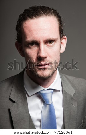Angry business man with long hair and expressive face wearing grey suit and blue tie. Isolated on grey background.