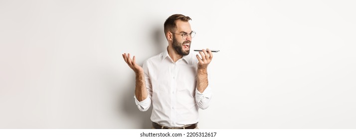 Angry Business Man Shouting At Speakerphone, Record Voice Message In Mad State, Standing Against White Background