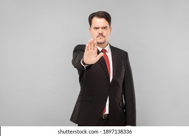 Angry Business Man Showing Hand. Stop This, Do Not Want To Listen Anymore, Go Out. Indoor Studio Shot. Isolated On Gray Background. Businessman With Black Suit, Red Tie And Mustache Looking At Camera