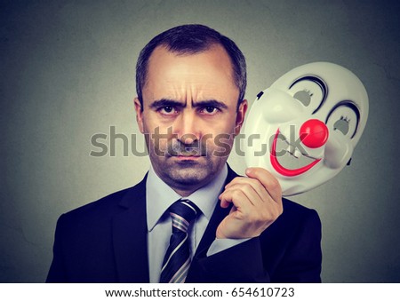 Angry business man taking off happy clown mask  