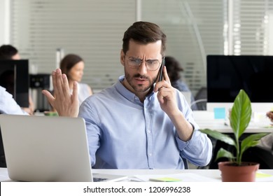 Angry Business Man Talking On Phone Disputing Looking At Laptop, Stressed Frustrated Office Worker Arguing By Mobile Solving Online Computer Problem With Technical Support Complaining On Bad Service