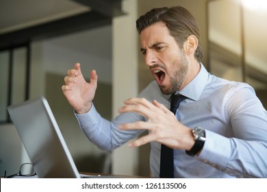 Angry Businessman Losing Patience And Screaming At Laptop In Modern Office