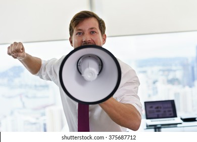Angry businessman with megaphone in modern office looking at camera. The angry man screams and fights for his labor rights. - Shutterstock ID 375687712