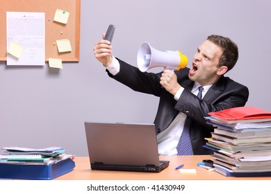 Angry businessman in an office, shouting on a megaphone, holding a mobile phone in the hand - Powered by Shutterstock