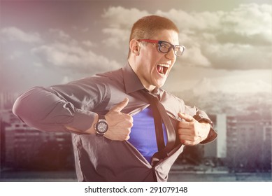 Angry Businessman Ripping Open His Shirt And Exposing A Superhero Blue Costume Underneath. The Man Is Wearing Glasses And Looking At Camera.