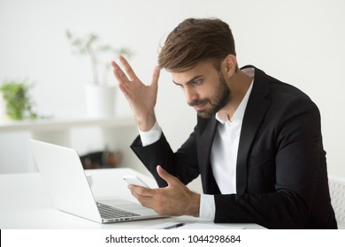 Angry businessman stressed about smartphone problem at workplace, frustrated executive feeling indignant annoyed about phone call, broken not working cell, received spam bad news in mobile message - Shutterstock ID 1044298684