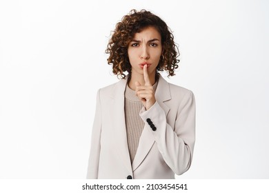 Angry Businesswoman Hushing, Making Shh Shush Taboo Gesture, Telling To Keep Quiet, Standing In Business Suit Over White Background