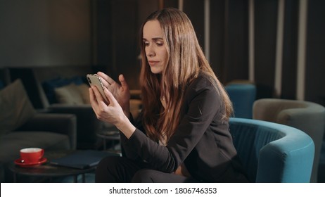 Angry Businesswoman Making Video Call Online On Mobile Phone In Hotel Lounge. Serious Woman Calling Video Chat On Smartphone In Hotel Lobby. Irritated Woman Using Phone For Online Video Call In Cafe