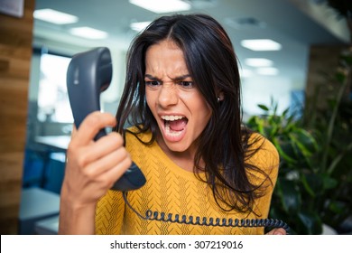 Angry businesswoman shouting on phone in office - Shutterstock ID 307219016