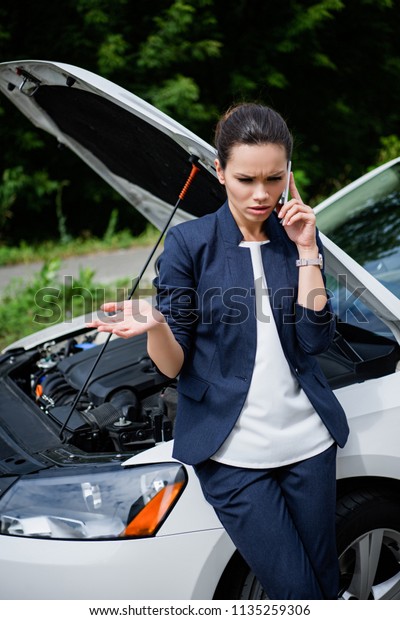 angry\
businesswoman talking by smartphone near broken\
car